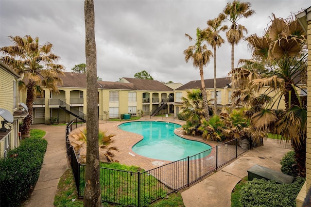 community pool featuring a patio, stairs, and fence