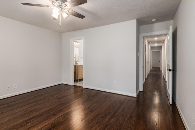 unfurnished bedroom featuring attic access, dark wood-style flooring, connected bathroom, a ceiling fan, and baseboards