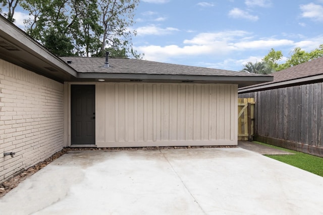 entrance to property featuring brick siding, a patio area, and roof with shingles