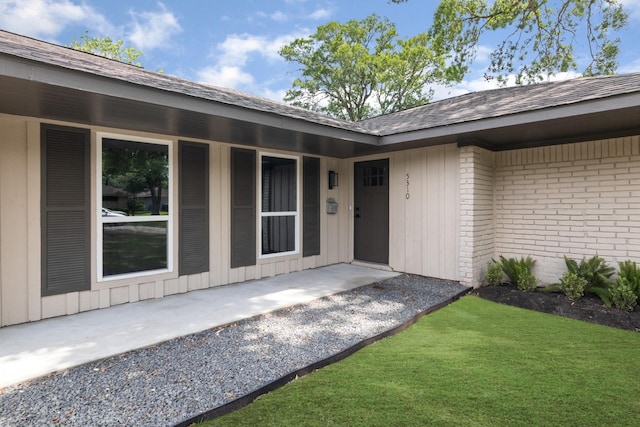 property entrance featuring brick siding, board and batten siding, and roof with shingles