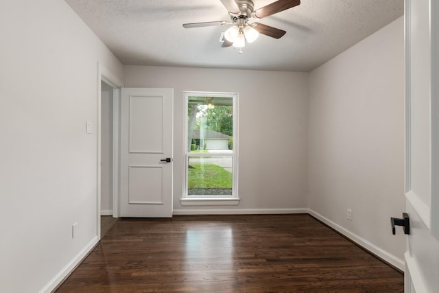 empty room with dark wood-type flooring, a ceiling fan, baseboards, and a textured ceiling
