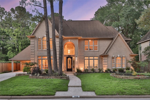 french provincial home featuring brick siding, fence, a front lawn, and concrete driveway