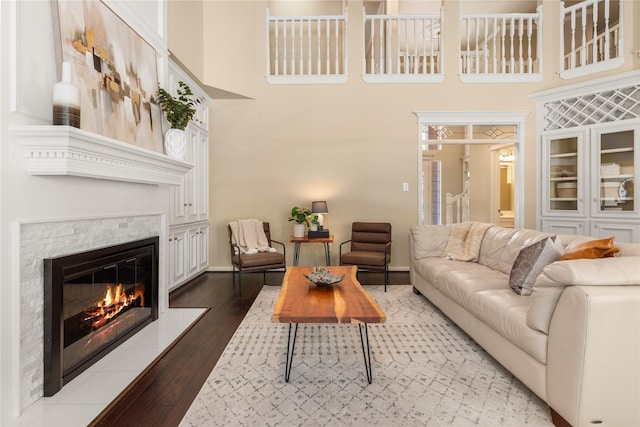 living area with a high ceiling, a tiled fireplace, wood finished floors, and baseboards