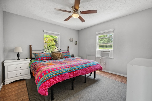 bedroom with cooling unit, multiple windows, wood finished floors, and baseboards