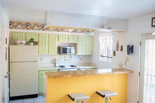 kitchen with light tile patterned floors, light countertops, a kitchen bar, white appliances, and a peninsula