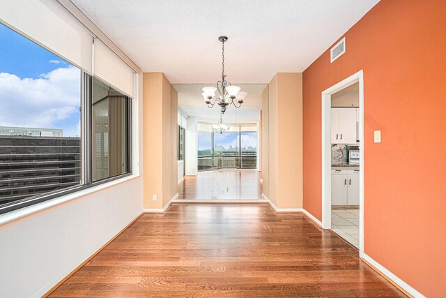 unfurnished dining area featuring baseboards, visible vents, wood finished floors, and an inviting chandelier