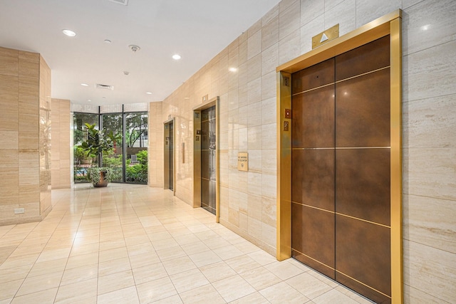 hall featuring recessed lighting, tile walls, light tile patterned floors, expansive windows, and elevator