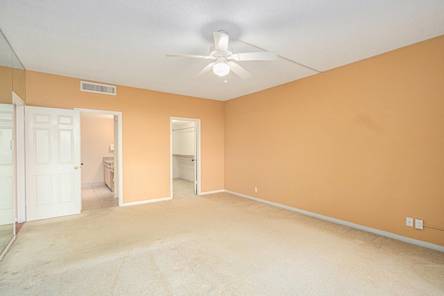 unfurnished bedroom with a closet, visible vents, light carpet, baseboards, and a spacious closet