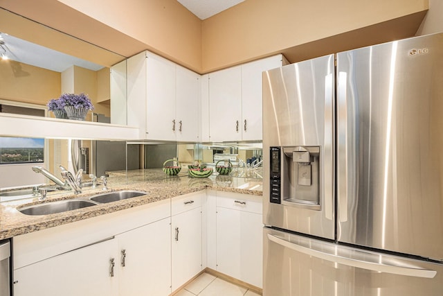 kitchen featuring light stone counters, white cabinetry, stainless steel fridge, and a sink