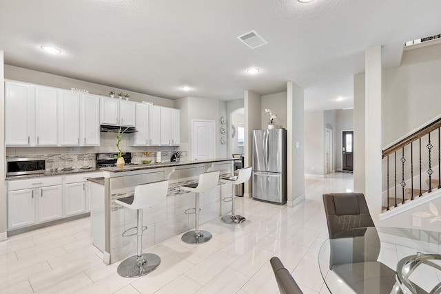 kitchen with under cabinet range hood, a kitchen bar, visible vents, backsplash, and appliances with stainless steel finishes