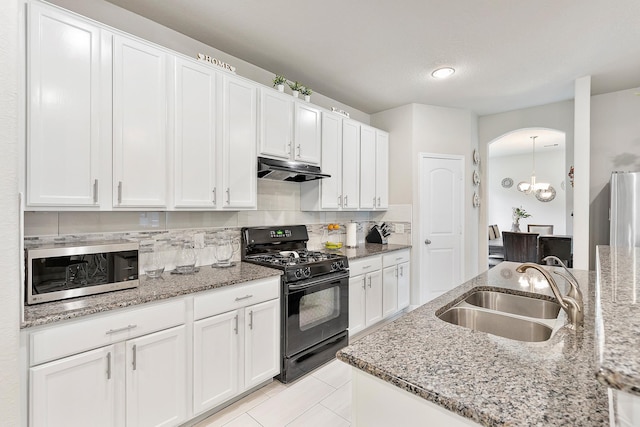 kitchen with stainless steel microwave, a sink, under cabinet range hood, arched walkways, and black range with gas cooktop