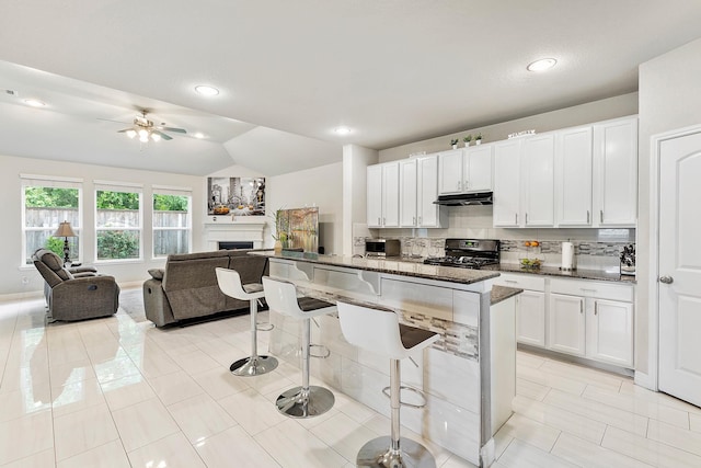 kitchen featuring white cabinets, under cabinet range hood, open floor plan, a kitchen bar, and gas stove