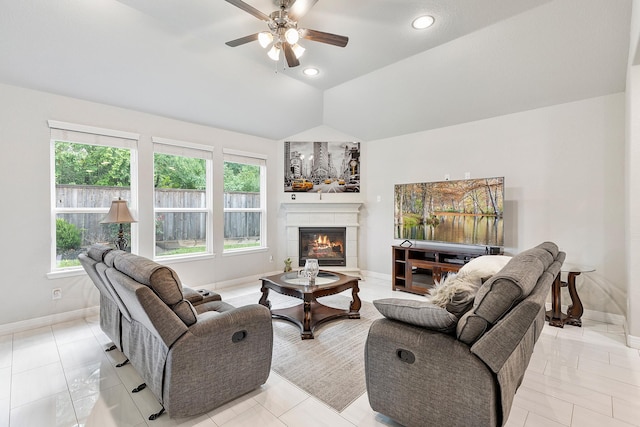 living room with a tile fireplace, a ceiling fan, vaulted ceiling, and baseboards