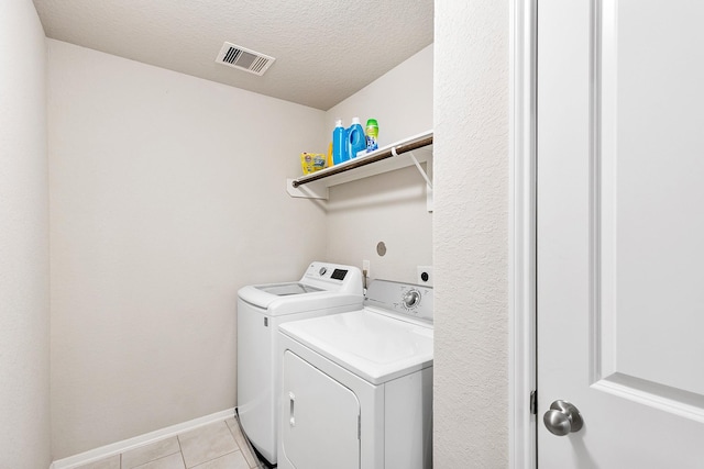 laundry area with light tile patterned floors, a textured ceiling, washing machine and dryer, visible vents, and laundry area