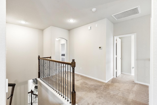 hallway with arched walkways, carpet floors, an upstairs landing, baseboards, and visible vents