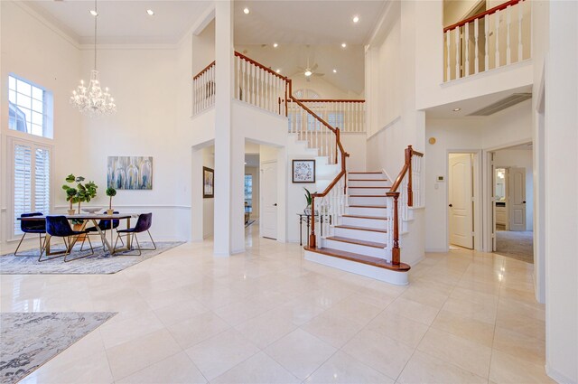 foyer featuring a high ceiling, ceiling fan with notable chandelier, baseboards, visible vents, and stairway