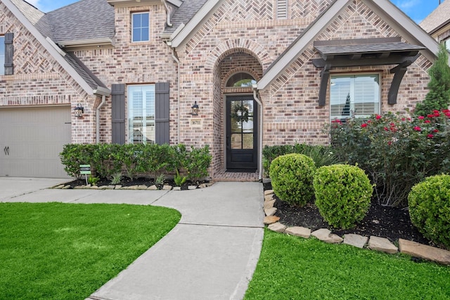16711 Arboleda Dr, Humble, TX 77346 - view of exterior entry with brick siding, a lawn, a garage, a shingled roof, and concrete driveway