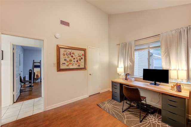 office space with light wood-style floors, high vaulted ceiling, baseboards, and visible vents