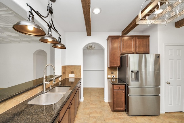 kitchen with dark stone counters, beamed ceiling, a sink, arched walkways, and stainless steel refrigerator with ice dispenser