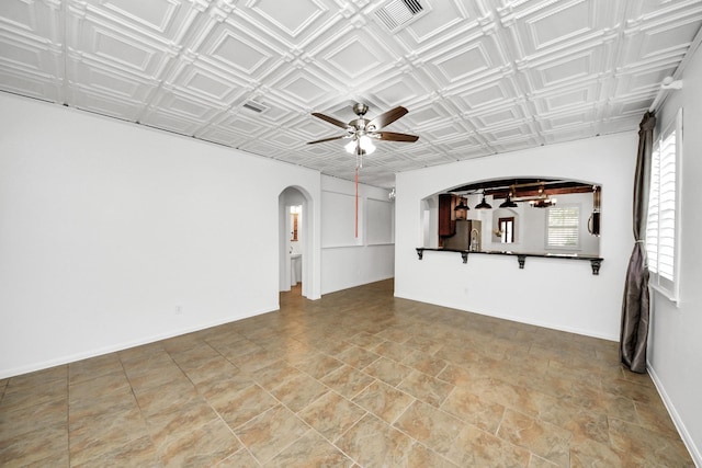 unfurnished living room featuring arched walkways, visible vents, a ceiling fan, and an ornate ceiling