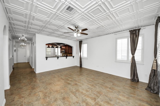 unfurnished living room featuring visible vents, arched walkways, ceiling fan with notable chandelier, and an ornate ceiling