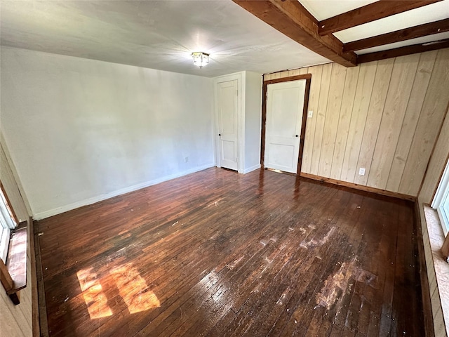 spare room featuring wood-type flooring, baseboards, wood walls, and beamed ceiling