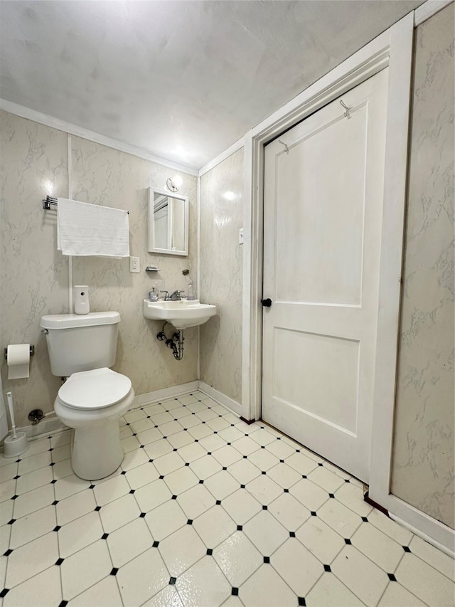 half bath featuring tile patterned floors, toilet, a sink, baseboards, and ornamental molding