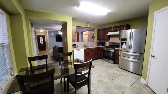 kitchen with under cabinet range hood, appliances with stainless steel finishes, light countertops, ceiling fan, and a sink