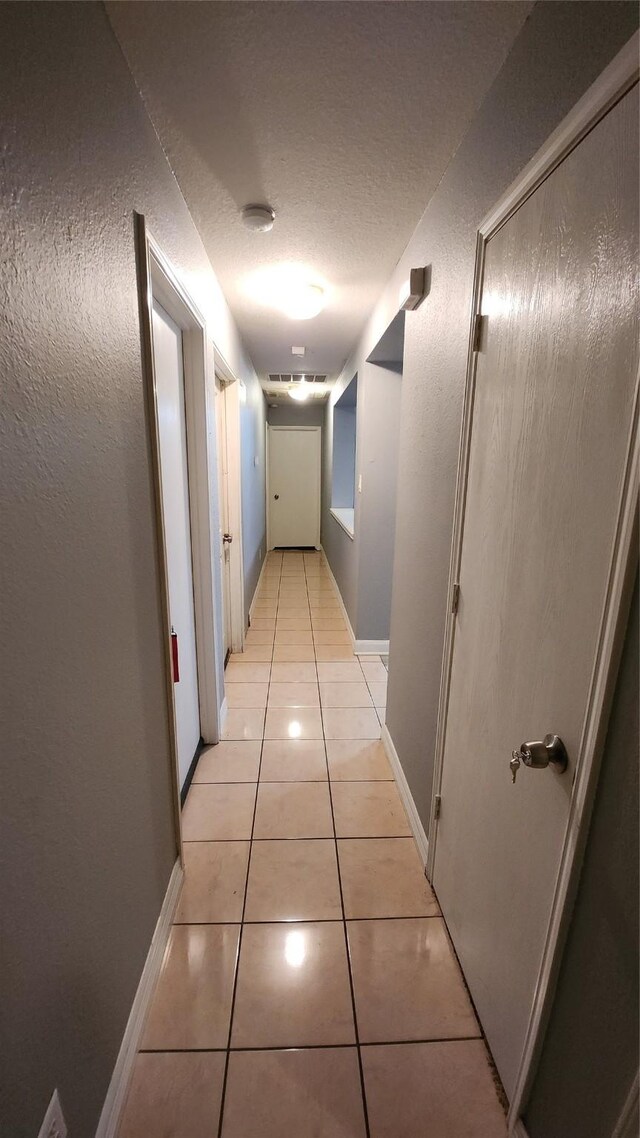 hall with light tile patterned floors, a textured ceiling, and baseboards