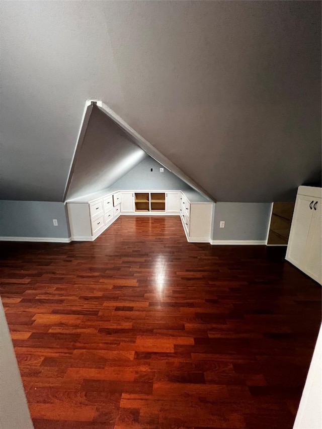 additional living space featuring dark wood-style floors, lofted ceiling, and baseboards