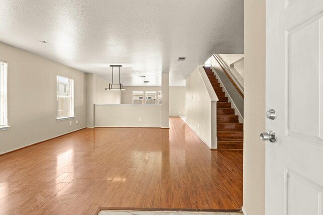 7931 Raven Creek Ln, Cypress, TX 77433 - unfurnished living room featuring a textured ceiling, visible vents, stairs, and wood finished floors
