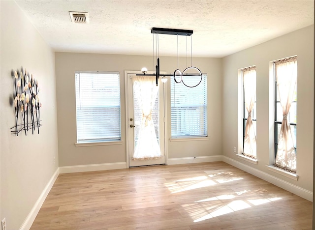 unfurnished dining area featuring a textured ceiling, visible vents, baseboards, an inviting chandelier, and light wood-type flooring