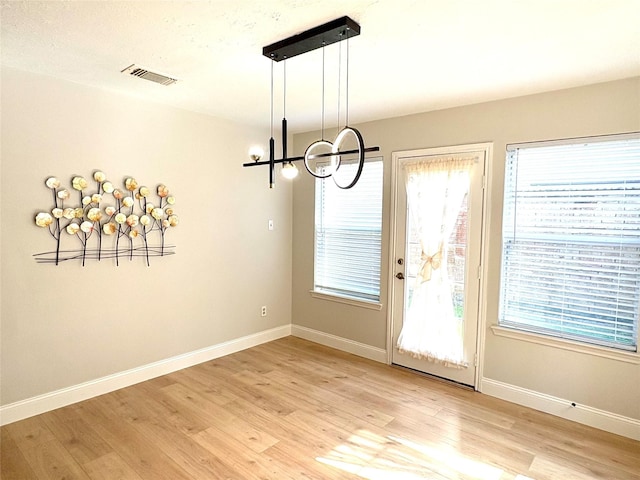 unfurnished dining area featuring visible vents, an inviting chandelier, baseboards, and light wood-style floors