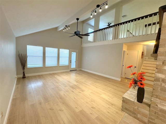 unfurnished living room with ceiling fan, rail lighting, light wood-type flooring, stairs, and baseboards