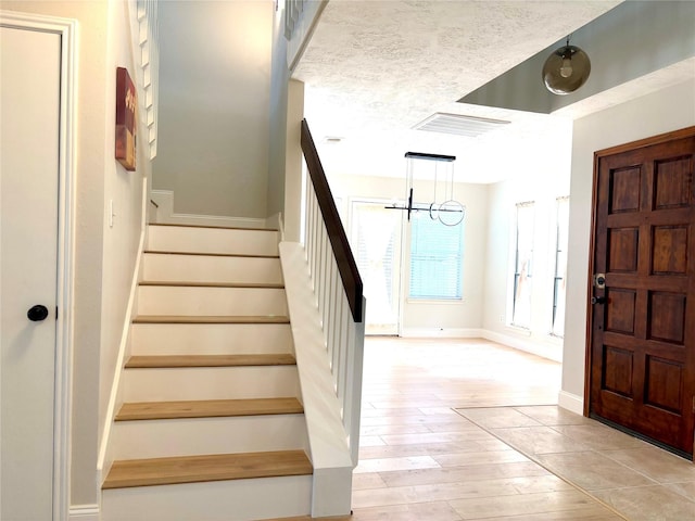 stairs with baseboards, visible vents, wood finished floors, and an inviting chandelier