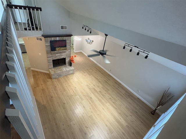 unfurnished living room with wood finished floors, a stone fireplace, baseboards, stairway, and a ceiling fan