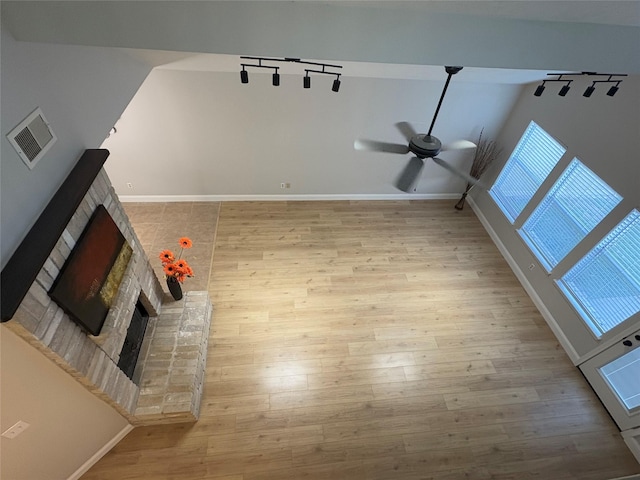 unfurnished living room with track lighting, wood finished floors, a fireplace with raised hearth, and a ceiling fan