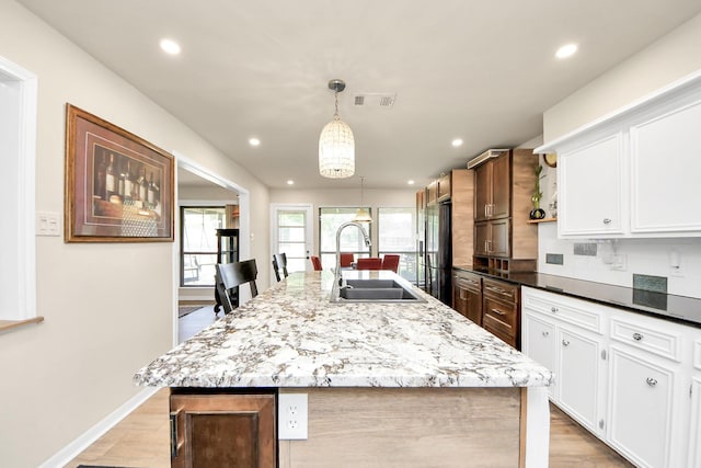 kitchen featuring light wood-style flooring, a sink, visible vents, an island with sink, and refrigerator with ice dispenser