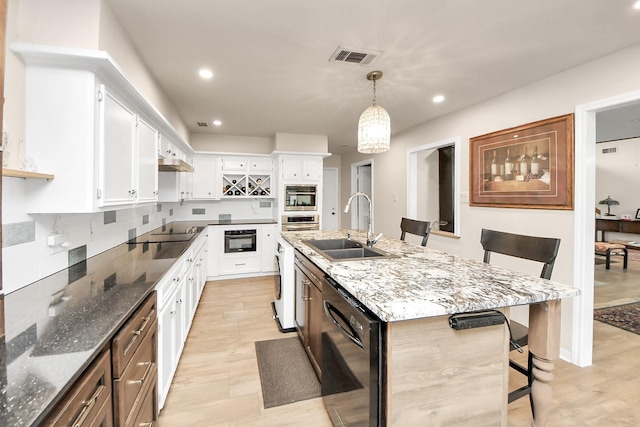 kitchen with dark stone countertops, black appliances, a sink, white cabinetry, and a kitchen breakfast bar