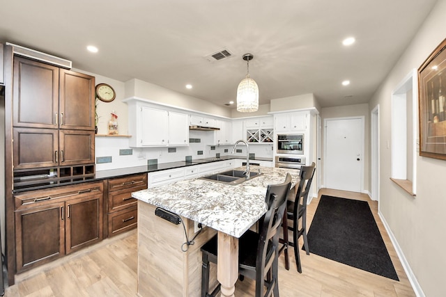 kitchen featuring visible vents, light wood-style flooring, stainless steel oven, and a sink