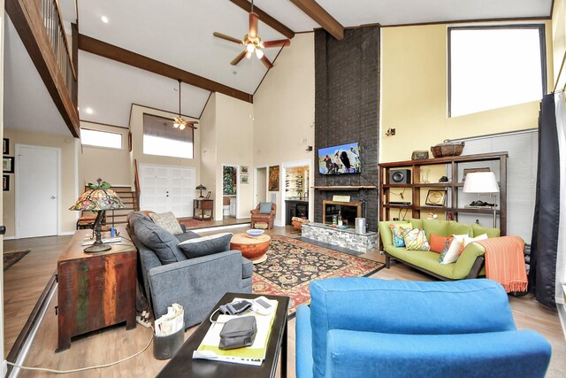living area featuring beam ceiling, a fireplace, wood finished floors, a ceiling fan, and high vaulted ceiling
