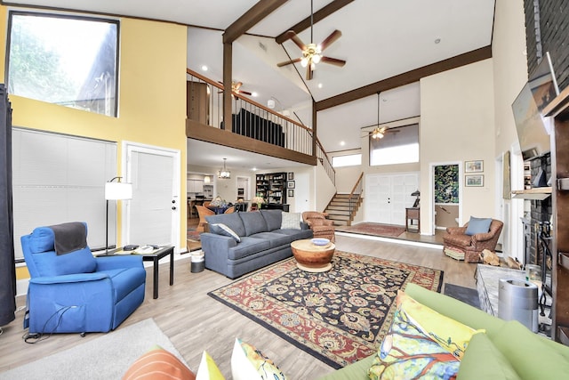 living area featuring beamed ceiling, ceiling fan, wood finished floors, high vaulted ceiling, and stairs