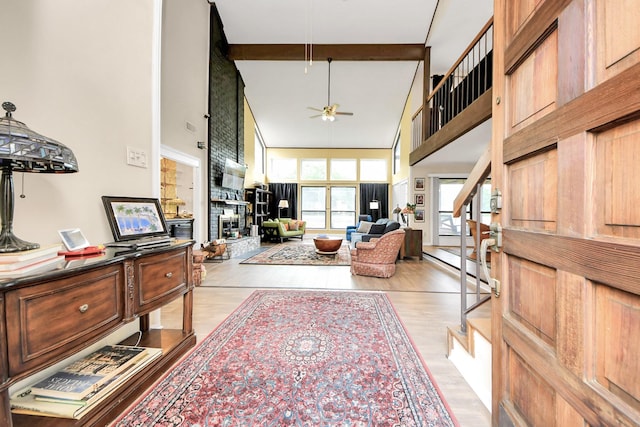living room with beamed ceiling, light wood-style floors, a glass covered fireplace, a ceiling fan, and a towering ceiling