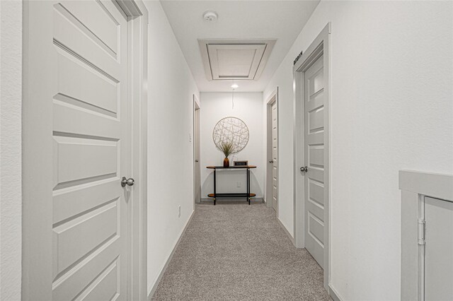 hall featuring baseboards, carpet, and attic access