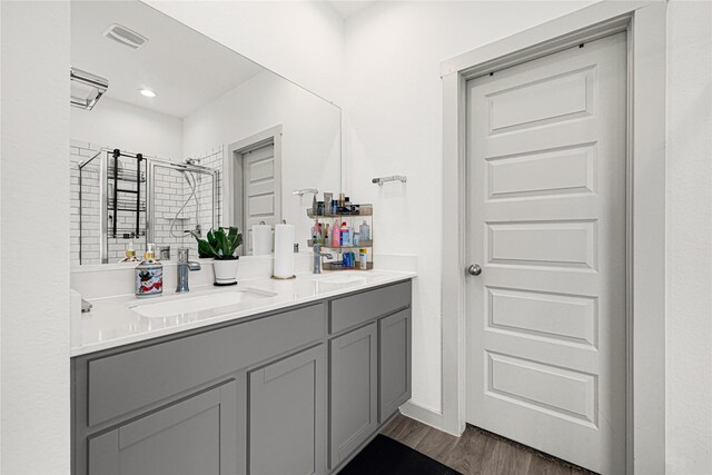 full bath featuring double vanity, visible vents, a shower stall, wood finished floors, and a sink