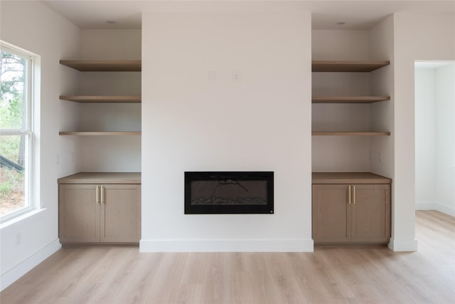 100 Mahalo Ct, Bastrop, TX 78602 - unfurnished living room with light wood-style floors, a glass covered fireplace, and baseboards