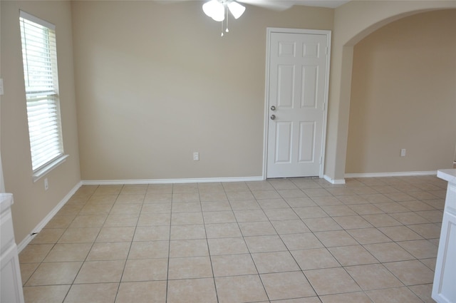 unfurnished room featuring light tile patterned floors, a ceiling fan, arched walkways, and baseboards