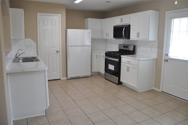 kitchen with light tile patterned floors, tasteful backsplash, a sink, freestanding refrigerator, and stainless steel range with gas stovetop