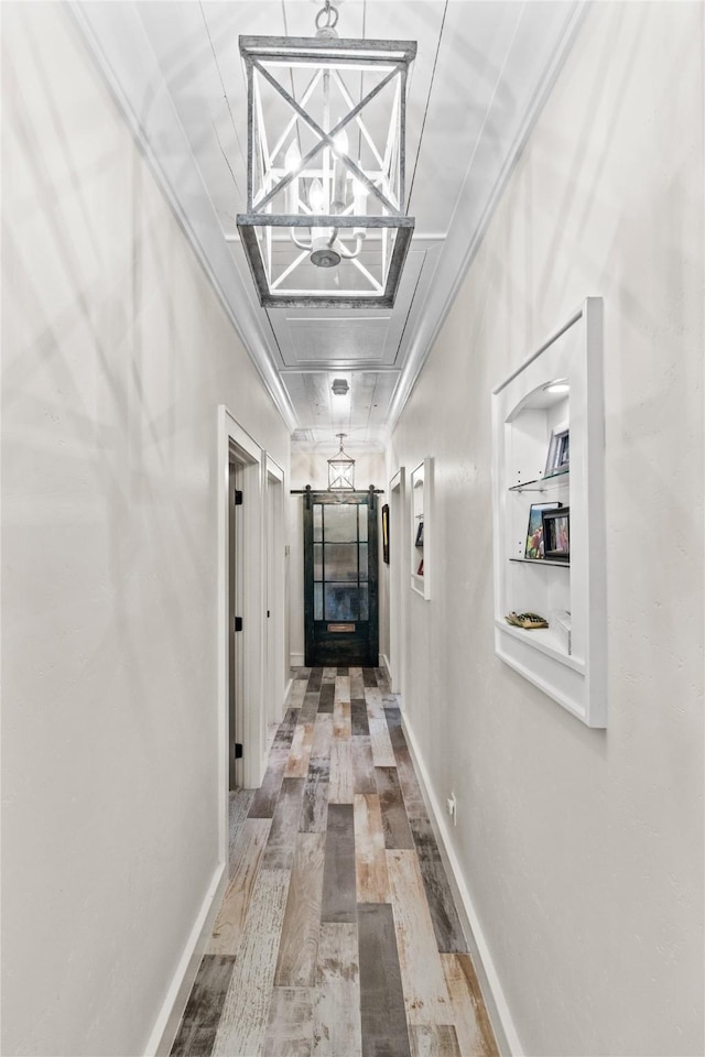 hall with baseboards, a barn door, wood finished floors, and ornamental molding