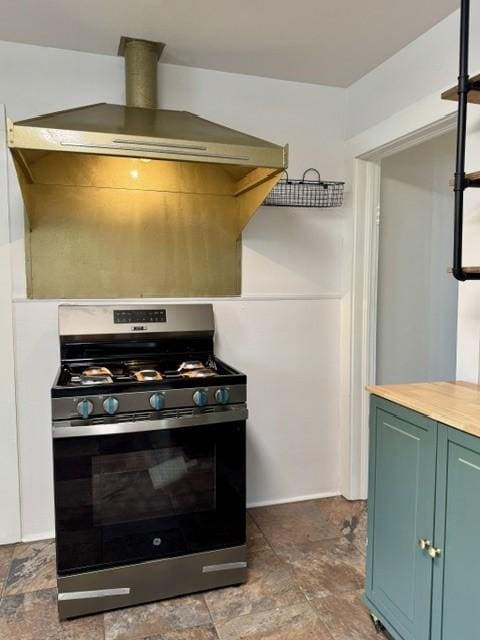 kitchen featuring blue cabinetry, green cabinetry, stone finish floor, wall chimney range hood, and gas stove